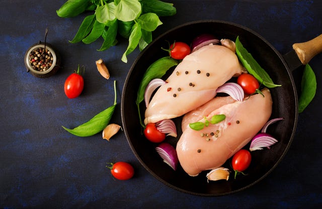 Raw chicken fillet prepared for baking in a pan on a dark background. Top view