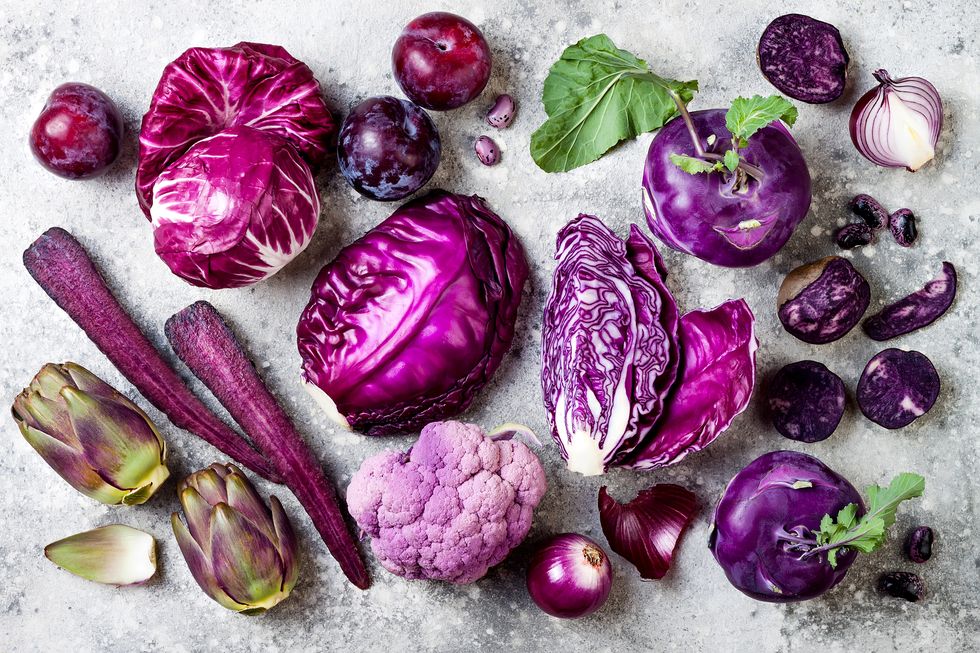 raw purple vegetables over gray concrete background cabbage, radicchio salad, olives, kohlrabi, carrot, cauliflower, onions, artichoke, beans, potato, plums top view, flat lay