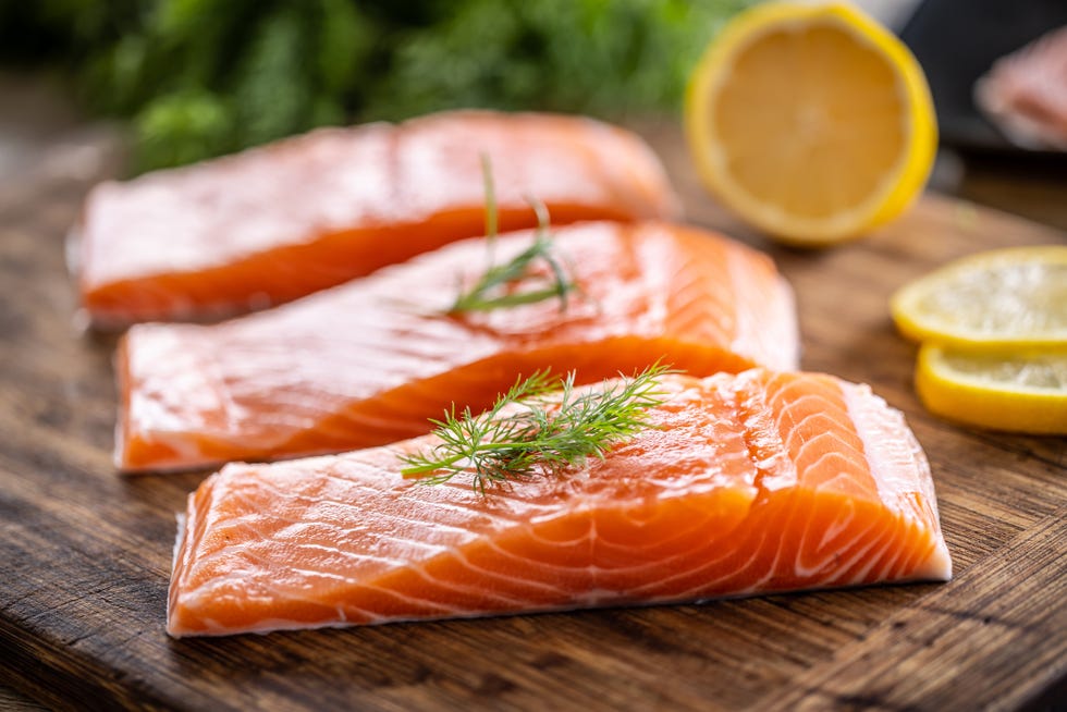 raw salmon fillets onwooden cutting board with dill, rosemary and lemon