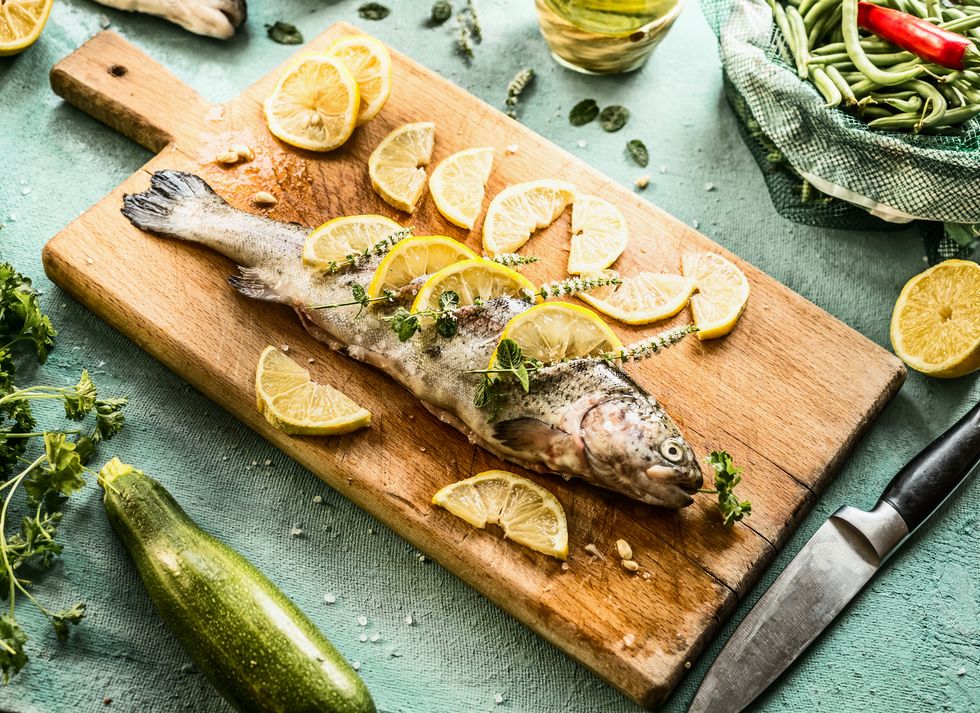raw trout fish on cutting board stuffed with herbs and lemon slices