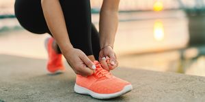Close up of sporty woman tying shoelace while kneeling outdoor, In background bridge. Fitness outdoors concept.