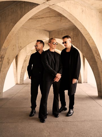 three individuals in formal attire standing under a concrete archway