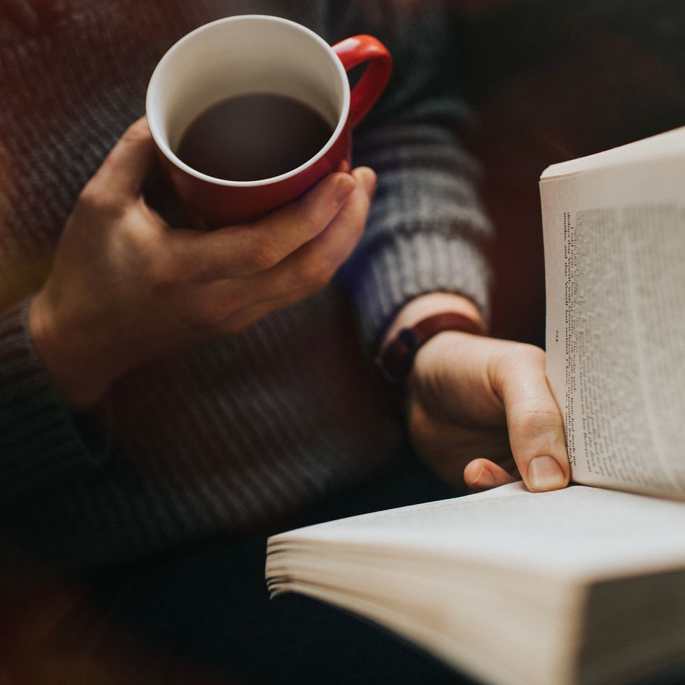 male reading a book and drinking a hot drink from a red mug cozy image