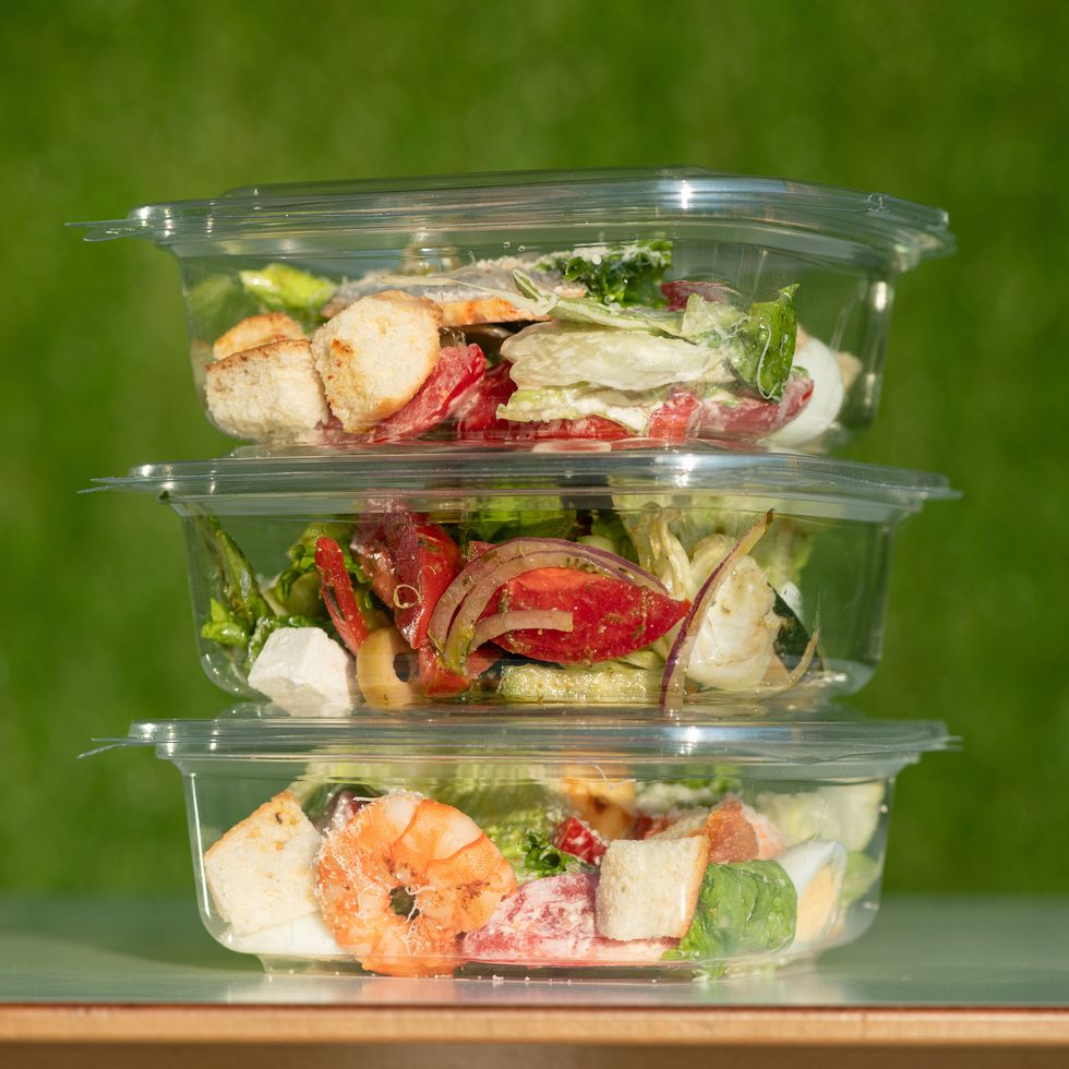 ready to eat food, three transparent plastic containers with salads on green background tower from disposable tableware with healthy eating side view