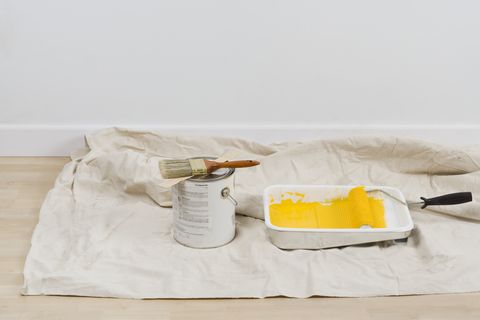 yellow paint in a roller tray with a paint roller on top of a canvas drop cloth