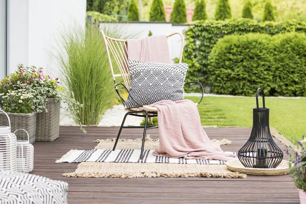 real photo of a white pillow and pink blanket on a rattan chair standing in the garden of a luxurious house