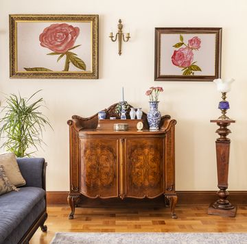 real photo of an antique cabinet with porcelain decorations, paintings with roses and blue sofa in a living room interior