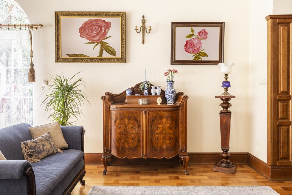real photo of an antique cabinet with porcelain decorations, paintings with roses and blue sofa in a living room interior