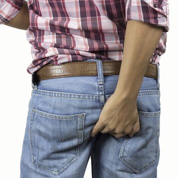 rear view midsection of man scratching buttocks against white background