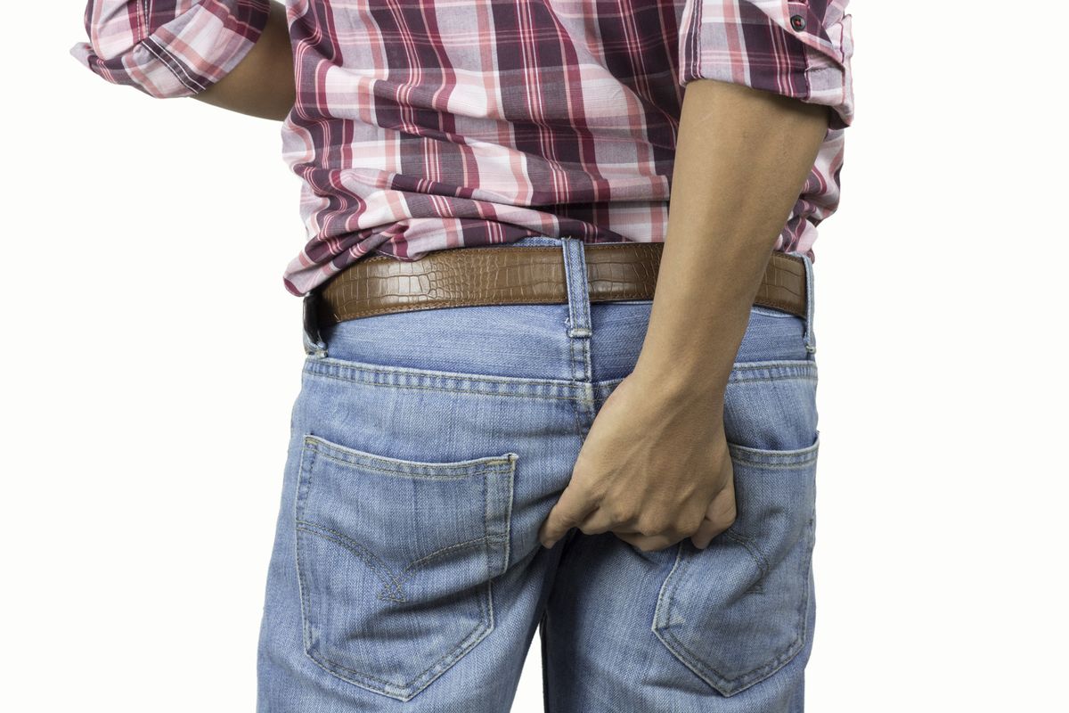 rear view midsection of man scratching buttocks against white background