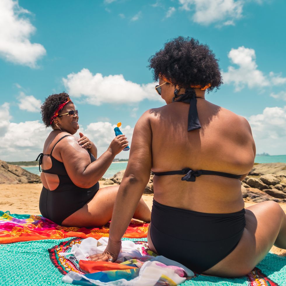 rear view of afro women using suntan lotion at beach