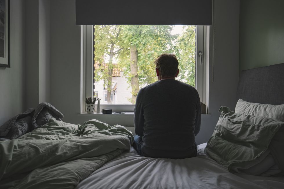 rear view of an unrecognisable mature man sitting on his bed looking out of the window negative emotion