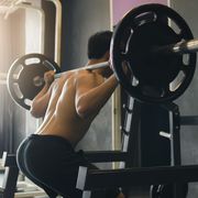 rear view of asian man performing barbell squats at the indoor gym