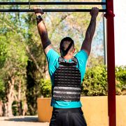 rear view of bearded brunette man doing a barbell pullup with weight vest outdoor fitness concept