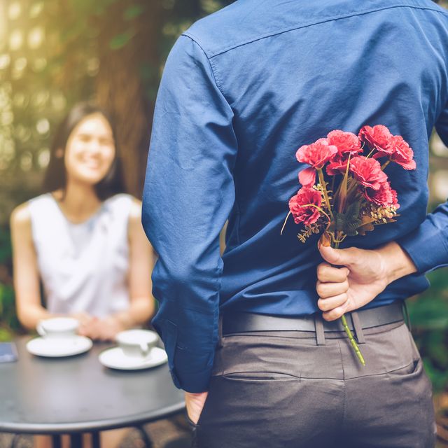 rear view of boyfriend hiding flowers while standing in front of girlfriend in garden