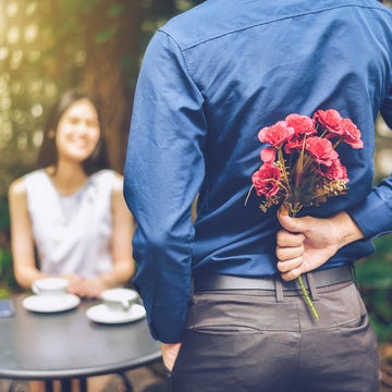 rear view of boyfriend hiding flowers while standing in front of girlfriend in garden