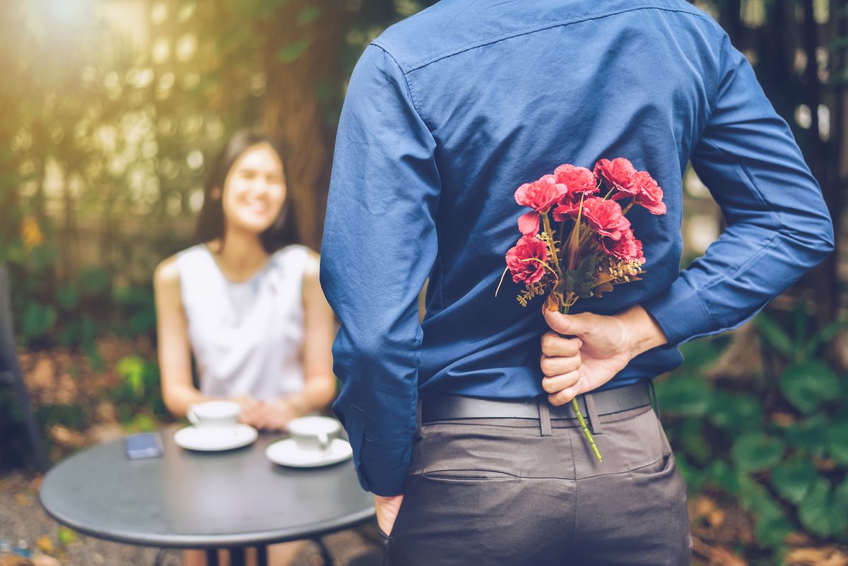 rear view of boyfriend hiding flowers while standing in front of girlfriend in garden