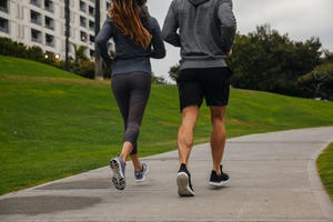 rear view of couple running on footpath in park