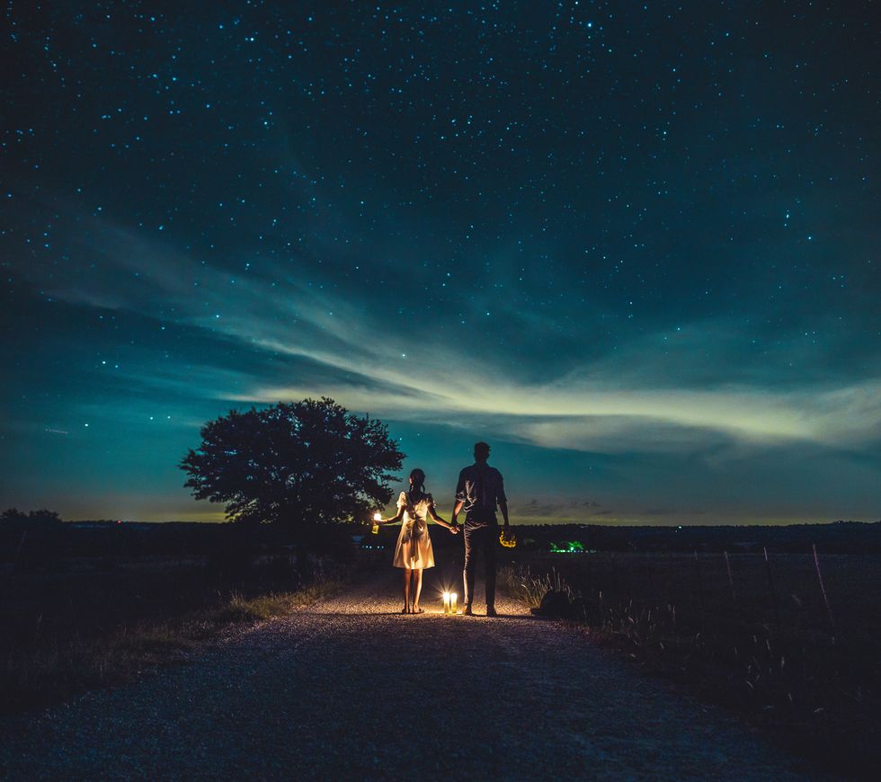 rear view of couple standing with illuminated lights on road against constellation