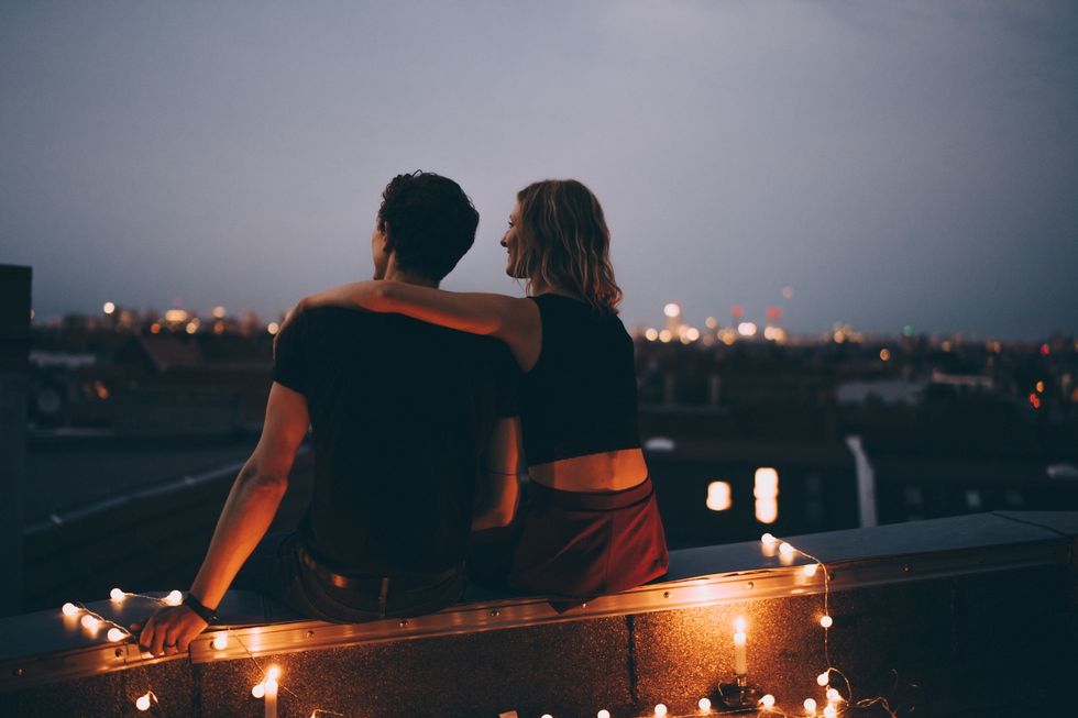 rear view of couple with arm around sitting on illuminated terrace in city against sky