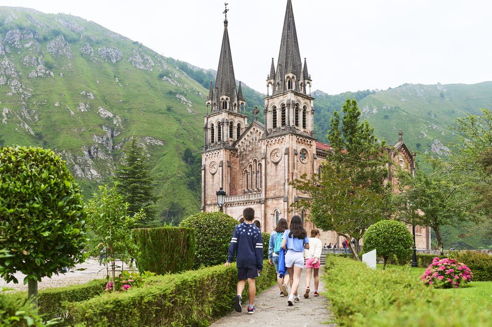 rear view of family group of people tourists with backpack and boys walking outside covadonga cathedral