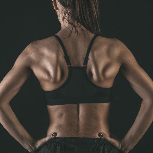 rear view of female athlete wearing sports bra standing with hands on hip against black background