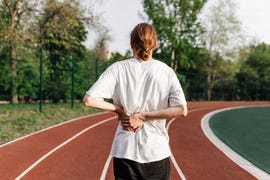 rear view of fit male athlete in white t shirt standing with his hands on his back on running track at stadium