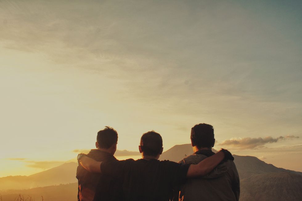 rear view of friends with arms around standing against sky during sunrise