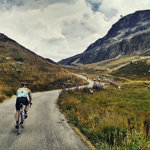 Rear View Of Man Cycling On Mountain Road Against Sky
