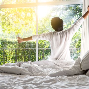 daylight saving sleep - Rear View Of Man Stretching Arms While Sitting On Bed At Home
