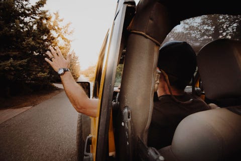 rear view of man waving through off road vehicle window while driving on road