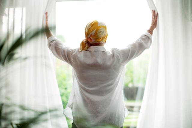 rear view of mature woman opening curtains at window