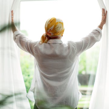 rear view of mature woman opening curtains at window