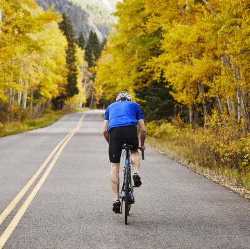 rear view of senior man riding bicycle on country road in forest
