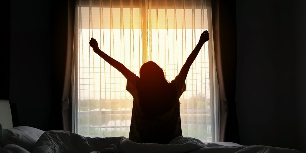 rear view of silhouette woman stretching hands while sitting on bed at home