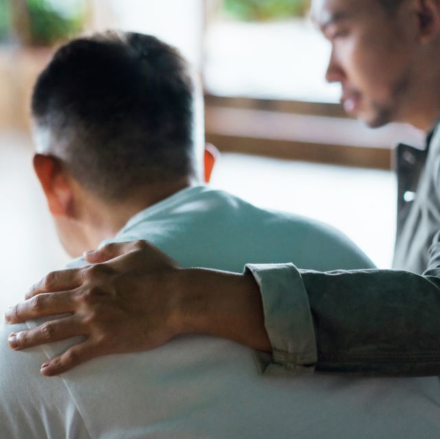 rear view of son and elderly father sitting together at home son caring for his father, putting hand on his shoulder, comforting and consoling him family love, bonding, care and confidence