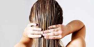rear view of woman applying conditioner on hair against white background