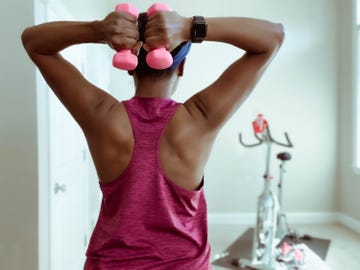 rear view of woman holding dumbbells behind head