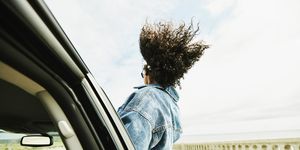 rear view of woman leaning out of car window with hair blowing in wind