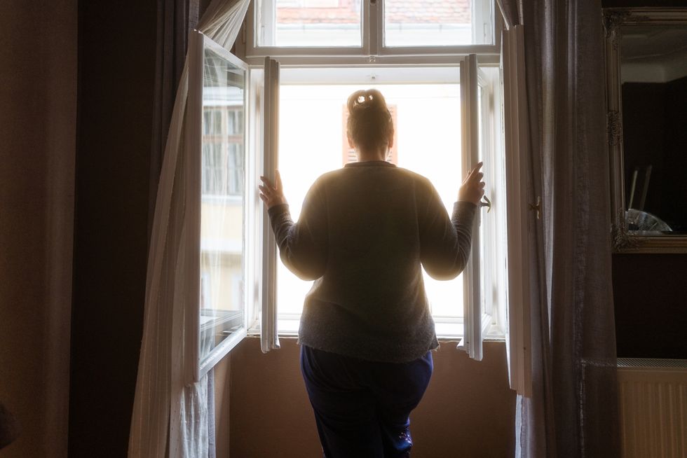rear view of woman looking at street from bedroom window