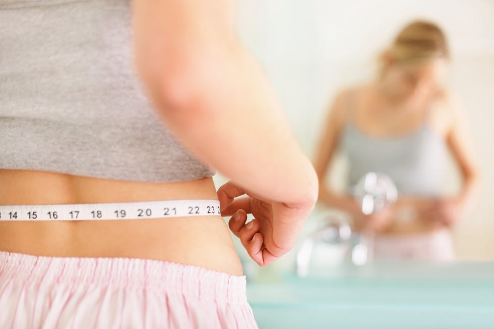 rear view of woman measuring waist with mirror reflection