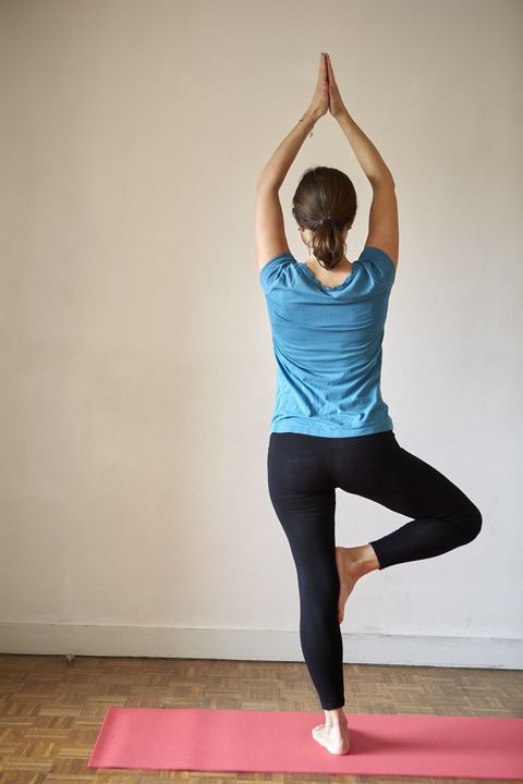 Rear view of woman on one leg, arms raised in yoga position
