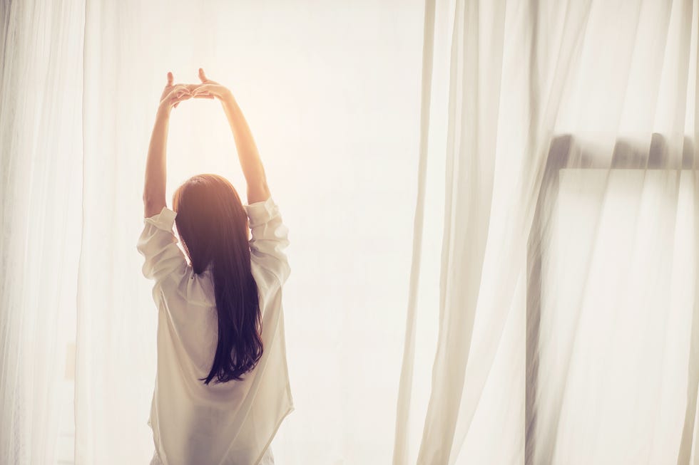 daylight saving sleep - Rear View Of Woman Stretching Hands Against Curtain