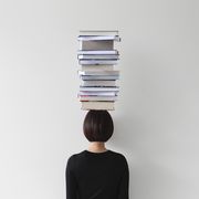 rear view of woman with stack of books on her head
