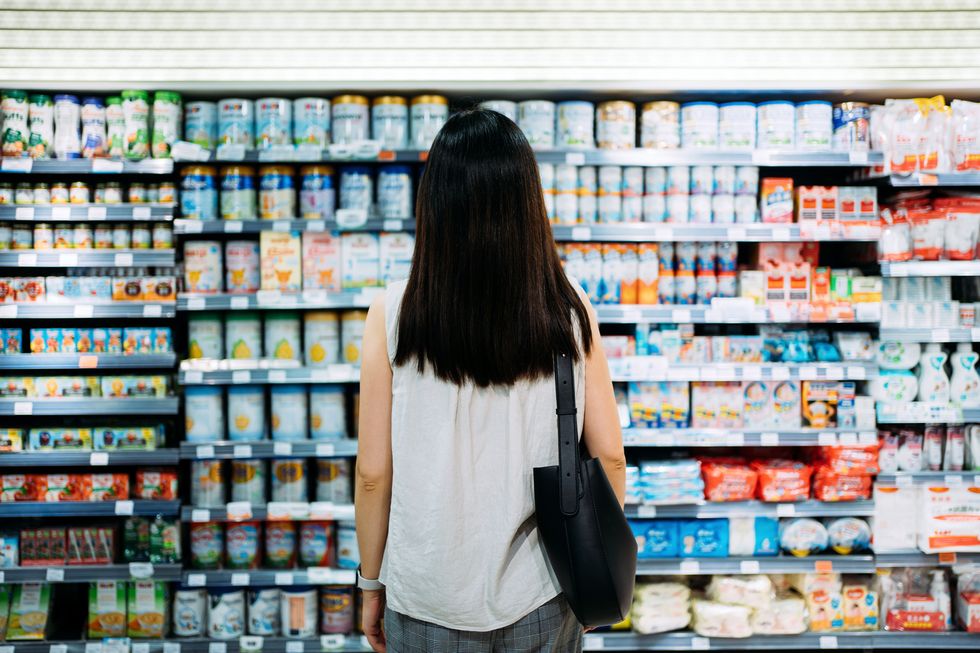 rear view of young asian mother groceries shopping for baby products in a supermarket she is standing in front of the baby product aisle and have no idea which product to choose from