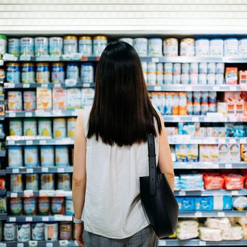 rear view of young asian mother groceries shopping for baby products in a supermarket she is standing in front of the baby product aisle and have no idea which product to choose from