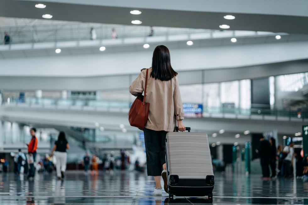 rear view of young asian woman carrying suitcase walking in airport terminal ready to travel travel and vacation concept business person on business trip