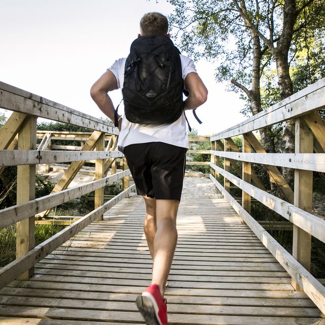 rear view of young male runner running across rural footbridge
