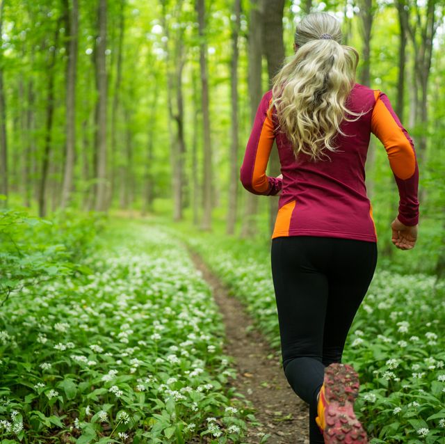 rear view woman jogging through forest in spring
