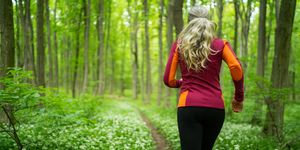 rear view woman jogging through forest in spring